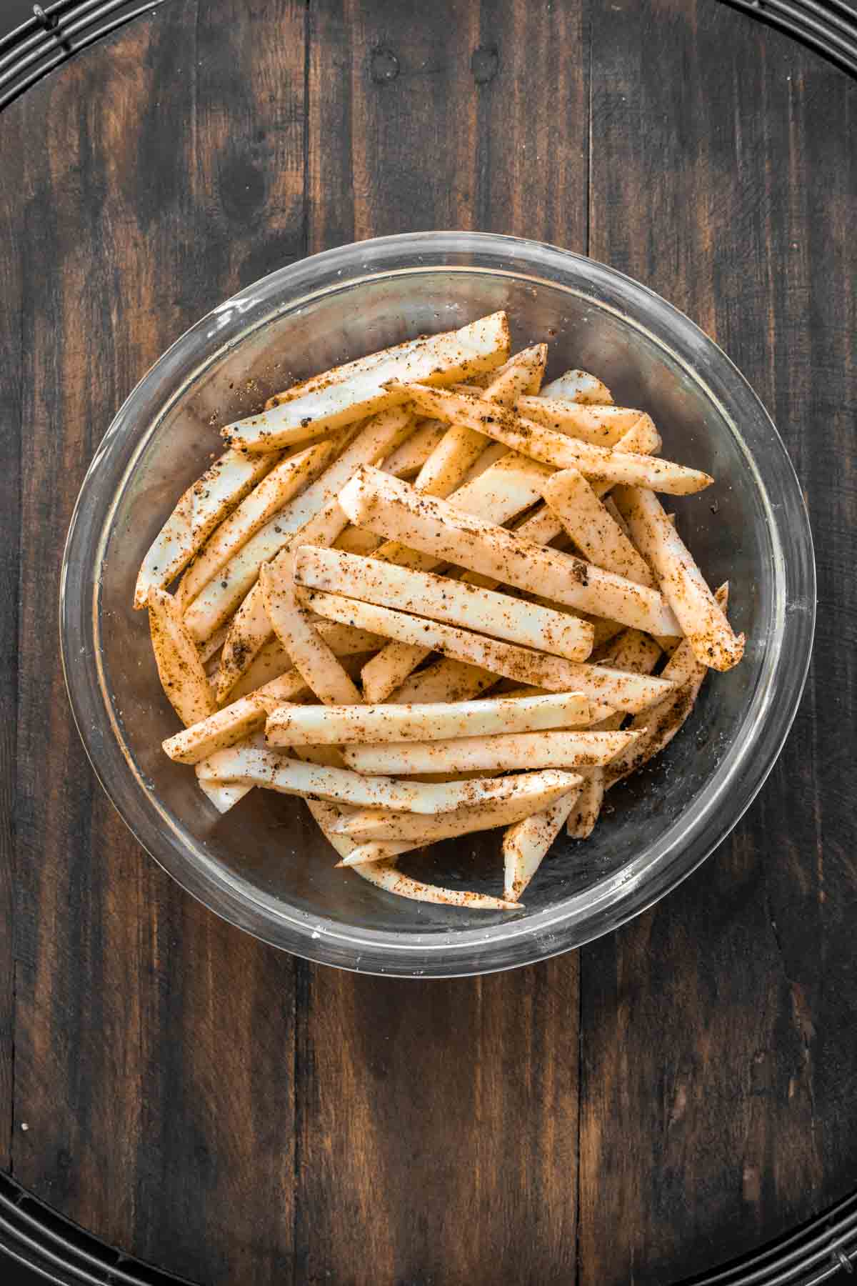 Cut white sweet potatoes in a glass bowl with seasonings.