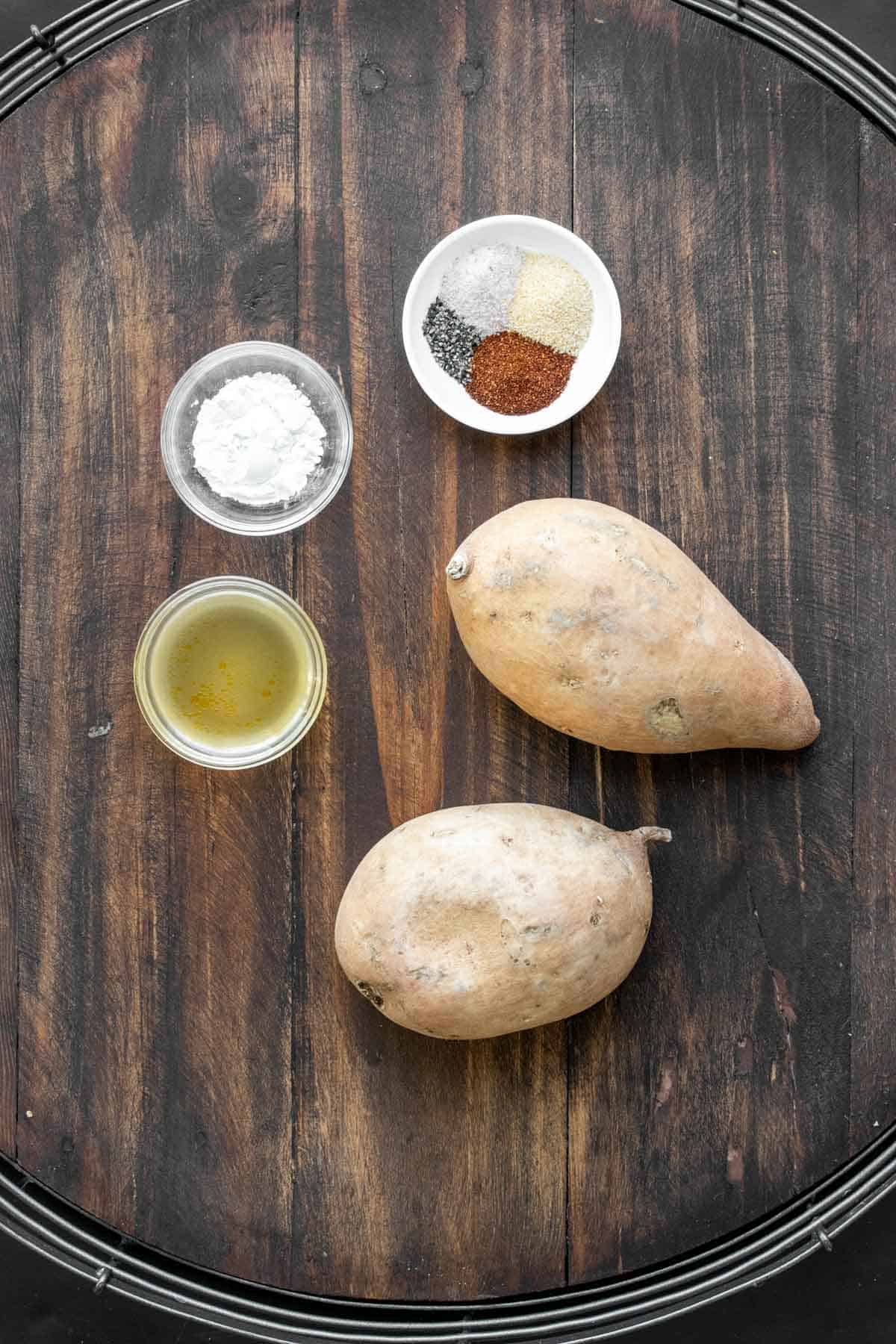 Two sweet potatoes and spices in bowls on a wooden surface