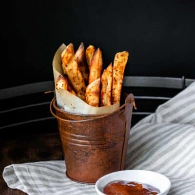Pail with parchment in a cone filled with sweet potato fries next to a bowl of ketchup