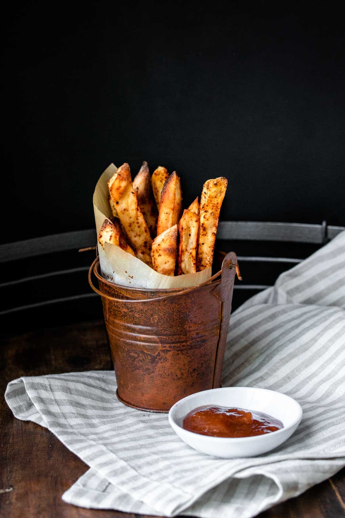 Pail with parchment in a cone filled with sweet potato fries next to a bowl of ketchup