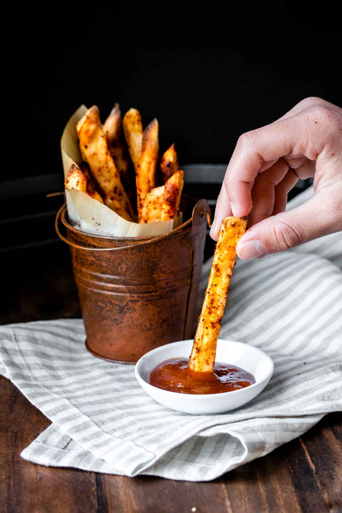 Hand dipping a sweet potato fry in a small bowl of ketchup.