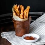 A brown pail with parchment in a cone filled with fries.