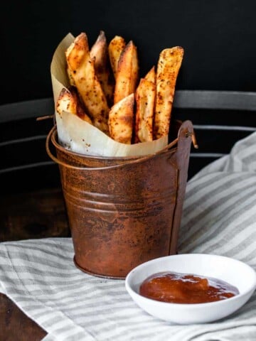 A brown pail with parchment in a cone filled with fries.