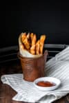 Sweet potato fries wrapped in parchment paper and sitting in a brown pail on a striped towel.