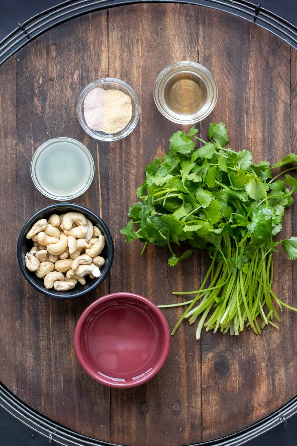 Bowls with cashews, lime juice, water, spices and vinegar next to a bunch of cilantro