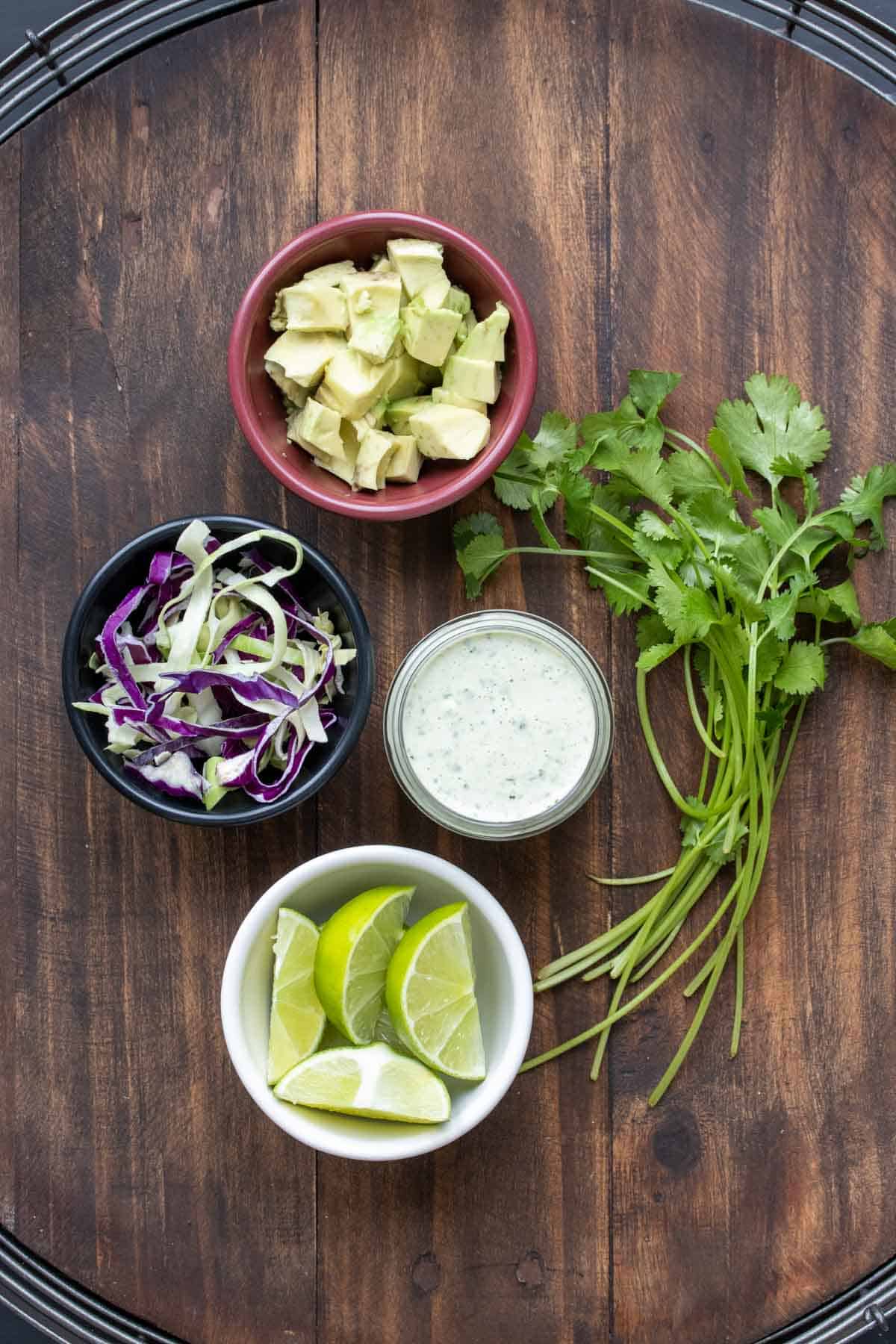 Toppings for tacos in bowls and a bunch of cilantro on a wooden surface