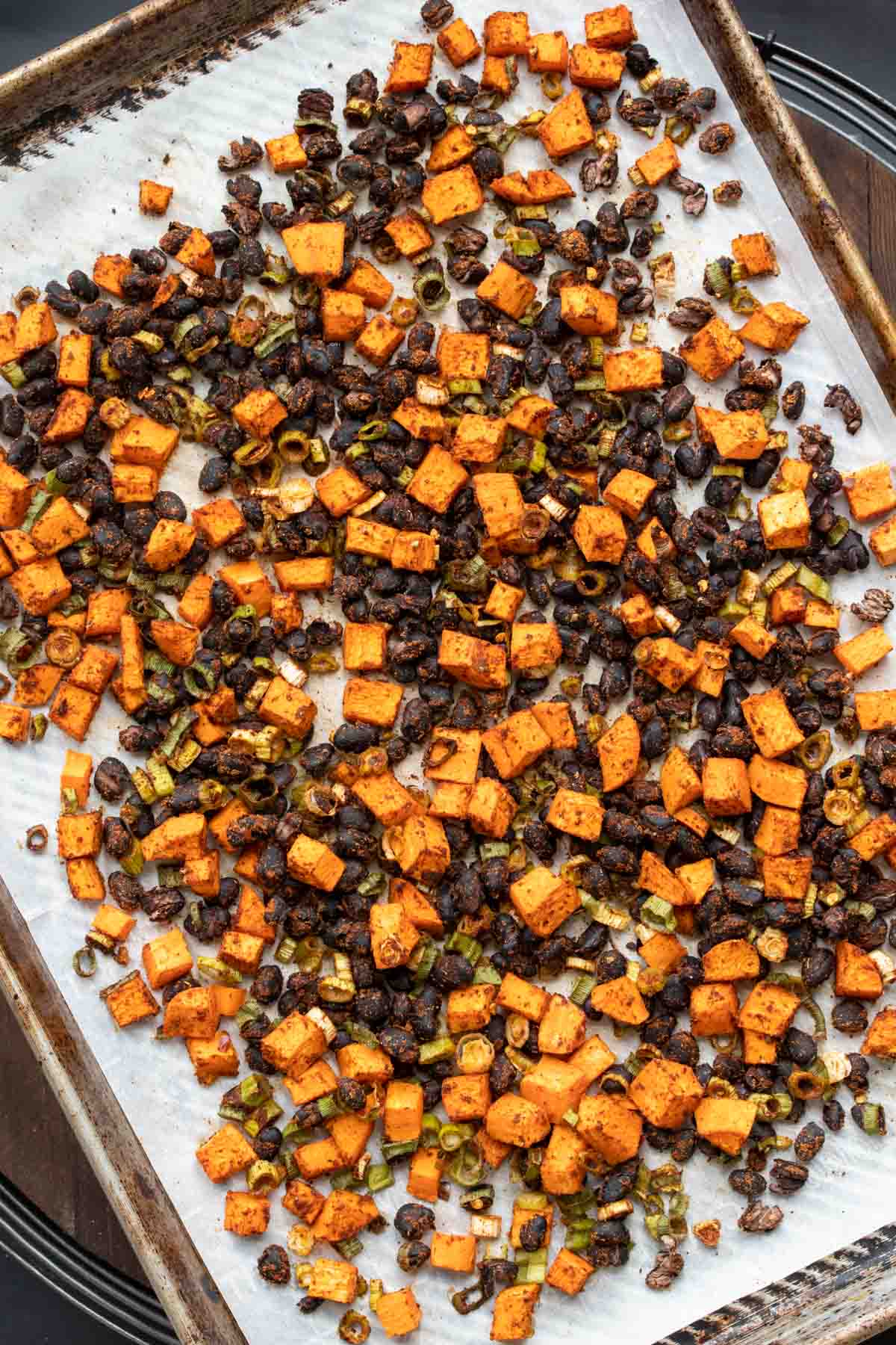 A sheet pan with parchment paper and baked sweet potato pieces and black beans