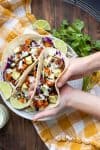 Hand holding a black bean and sweet potato taco over a plate of more tacos