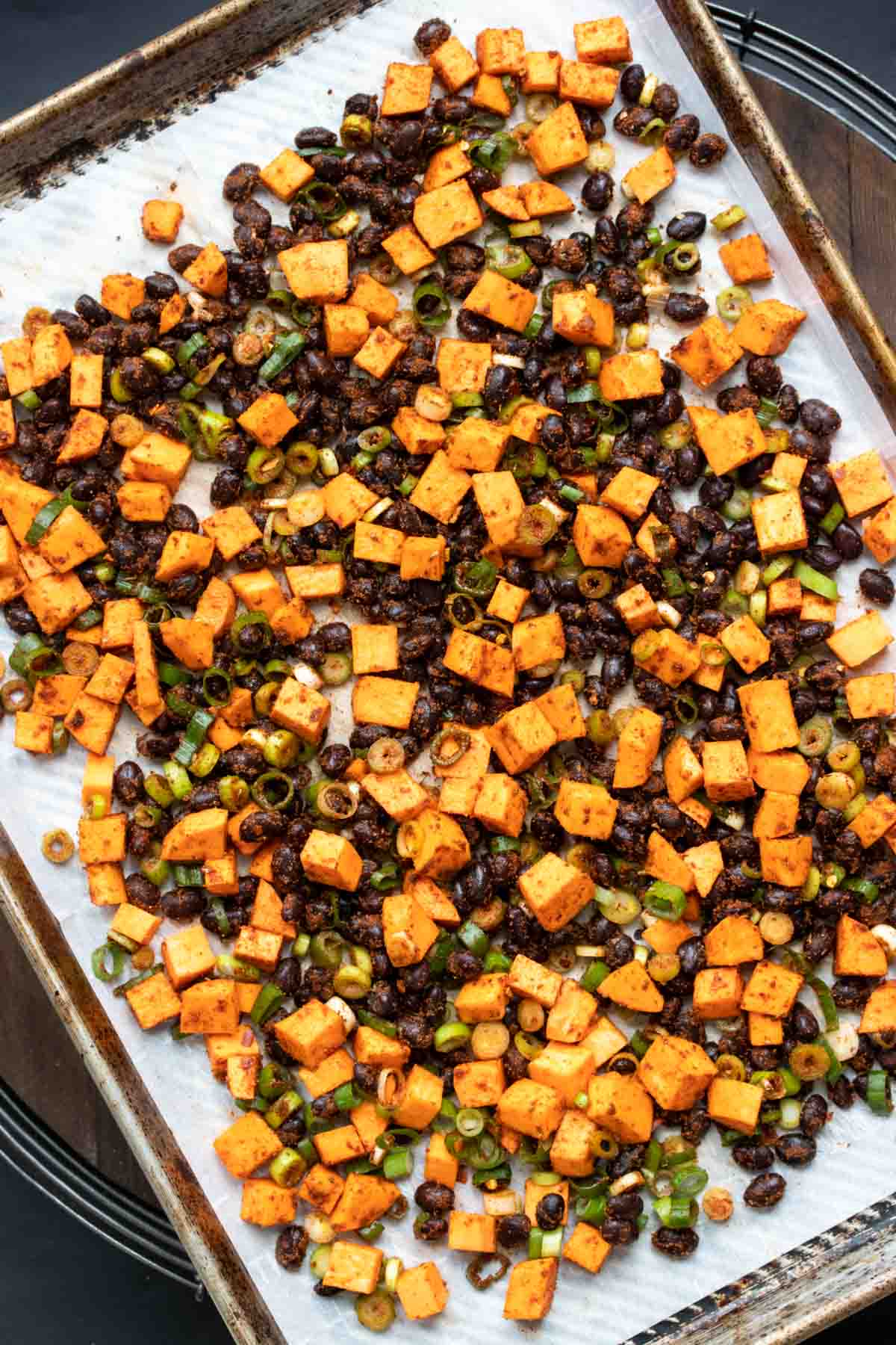 Pan with chopped sweet potato, black beans and green onion on parchment paper