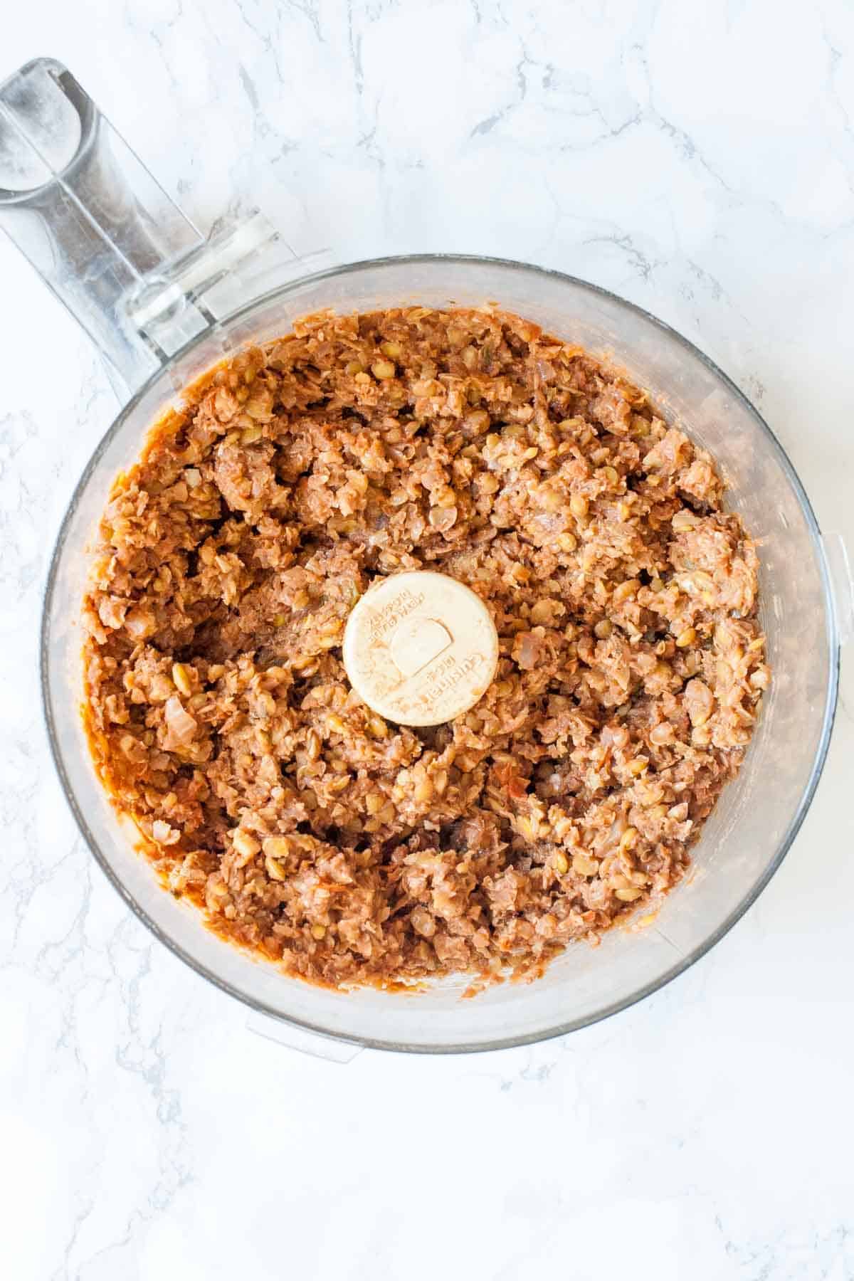 Top view of a food processor with chopped lentil meat in it.