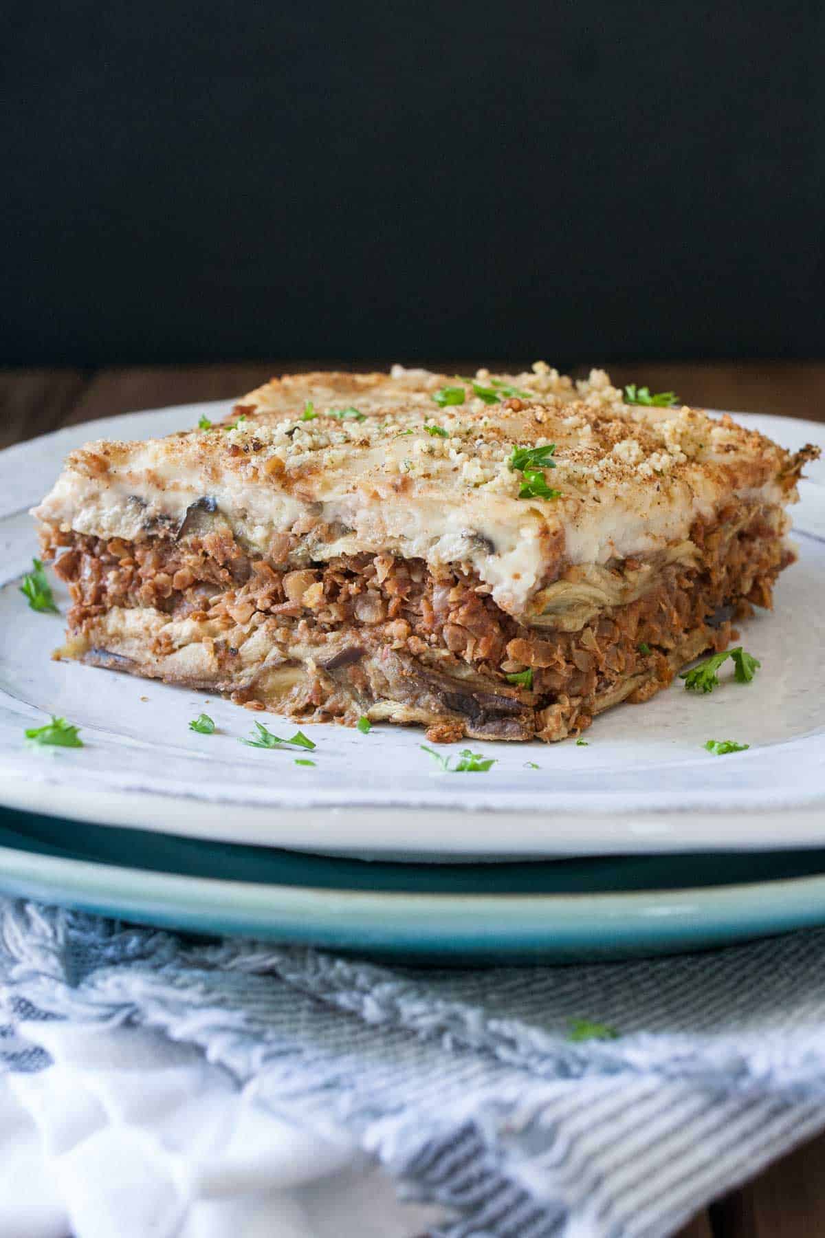White plate on top of a blue plate with a slice of lentil based moussaka on it