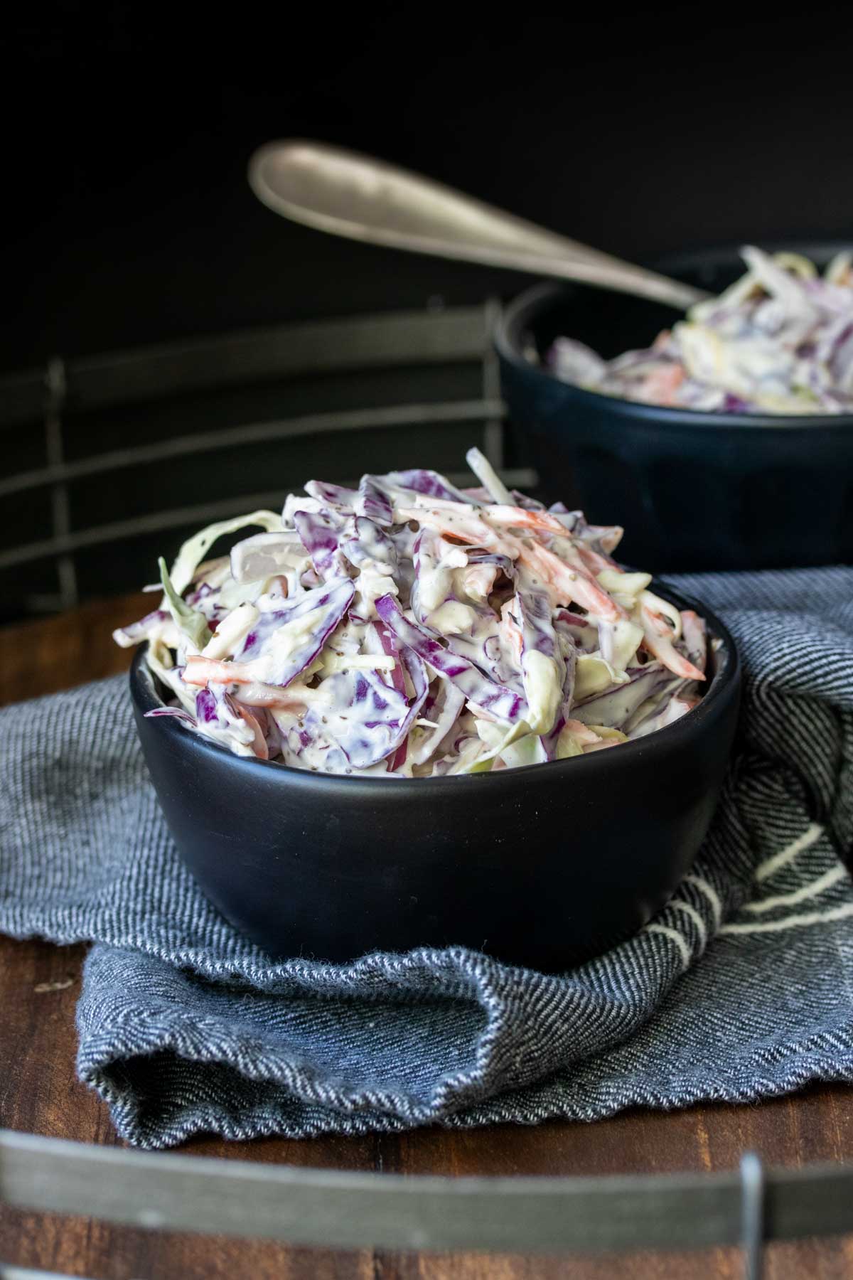 Black bowl filled with coleslaw on a blue napkin.