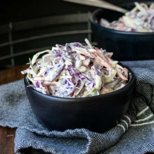 Creamy coleslaw in a black bowl that is sitting on top of a blue napkin.