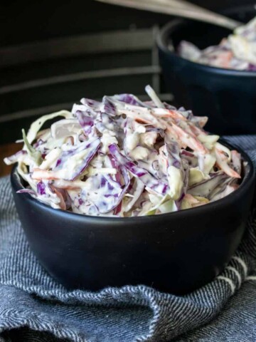 Creamy coleslaw in a black bowl that is sitting on top of a blue napkin.