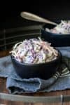 A photo of a black bowl in a grey towel filled with creamy coleslaw inside it.