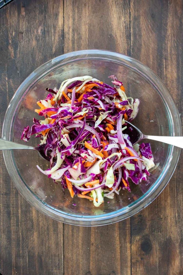 Glass bowl with shredded purple cabbage, carrots and red onion.