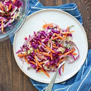 White plate piled with cabbage slaw with carrots and red onion in it.