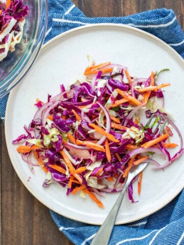 White plate piled with cabbage slaw with carrots and red onion in it.