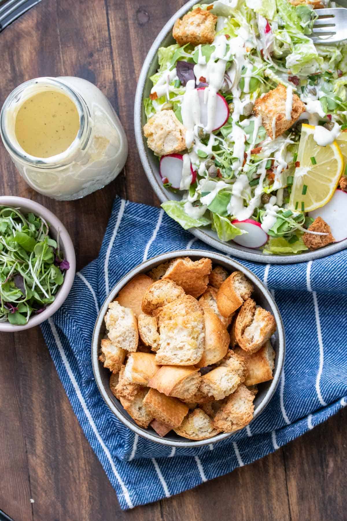 Top view of bowls of salad, croutons, microgreens and dressing