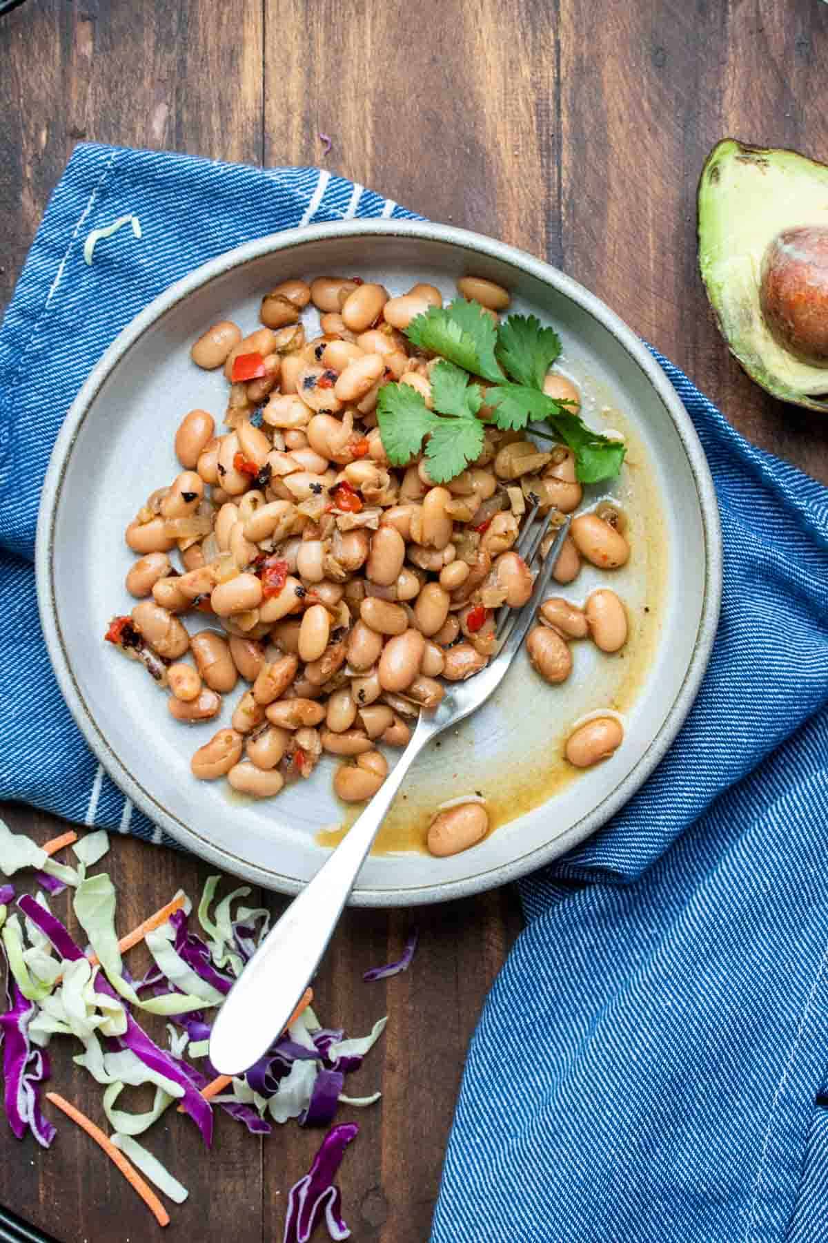 Grey plate filled with pinto beans and a spring of cilantro next to cabbage and an avocado