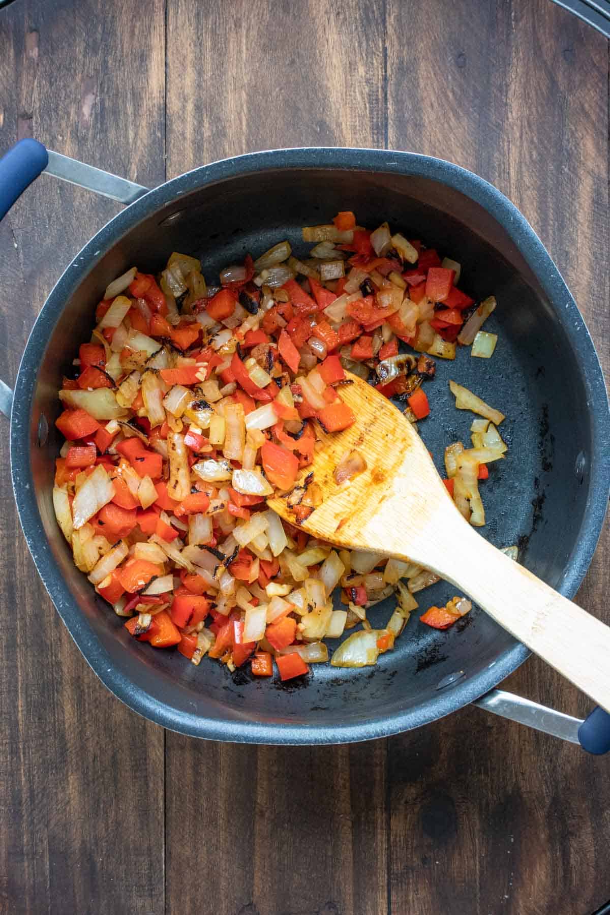 Wooden spoon mixing chopped red pepper and onion in a pot