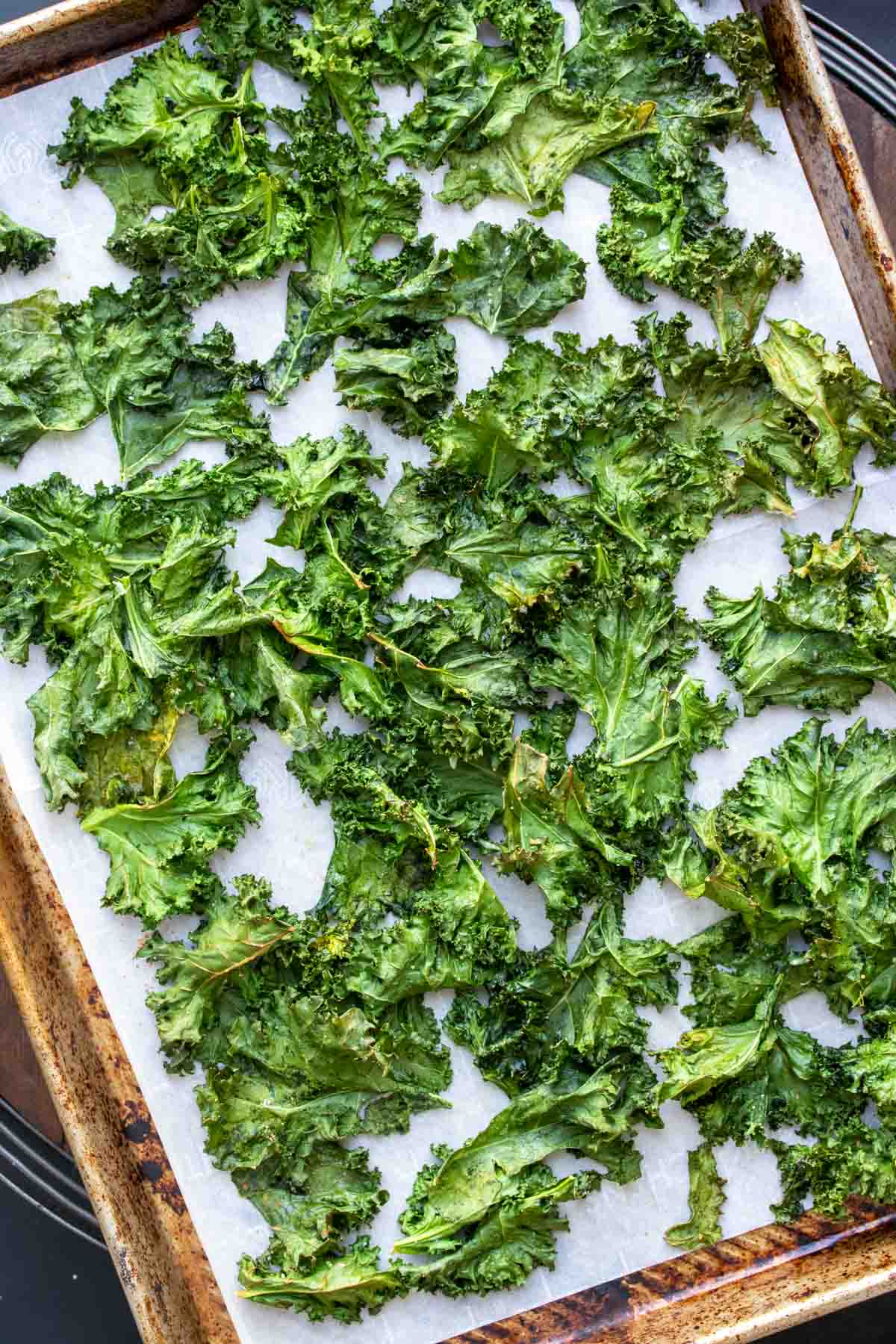 Baked kale chips spread on a parchment lined baking sheet