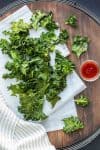 Wooden surface with parchment paper covered in a pile of kale chips