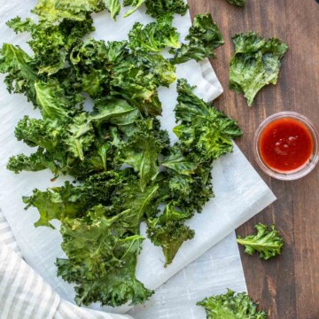 Wooden surface with parchment paper covered in a pile of kale chips