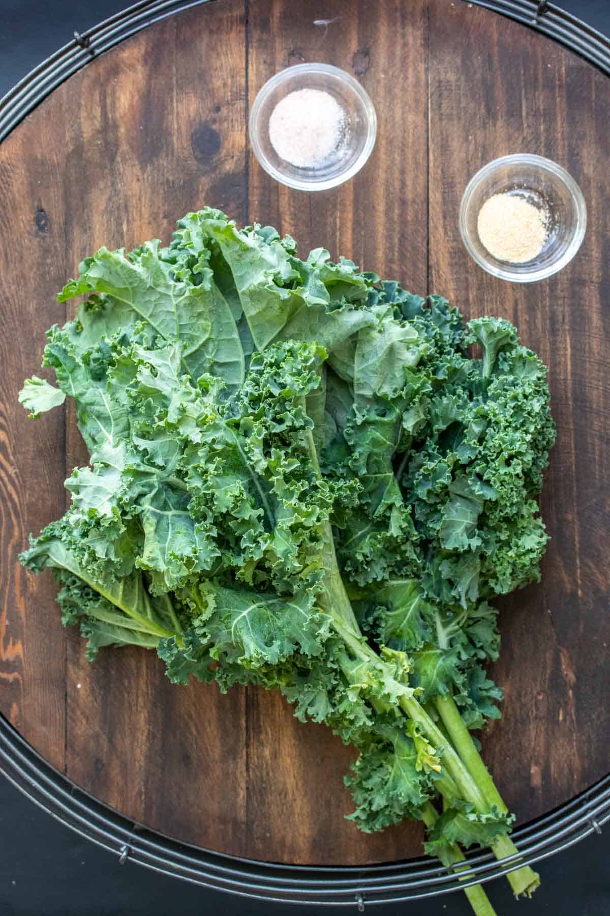 Wooden surface with a bunch of kale and little bowls of salt and garlic powder