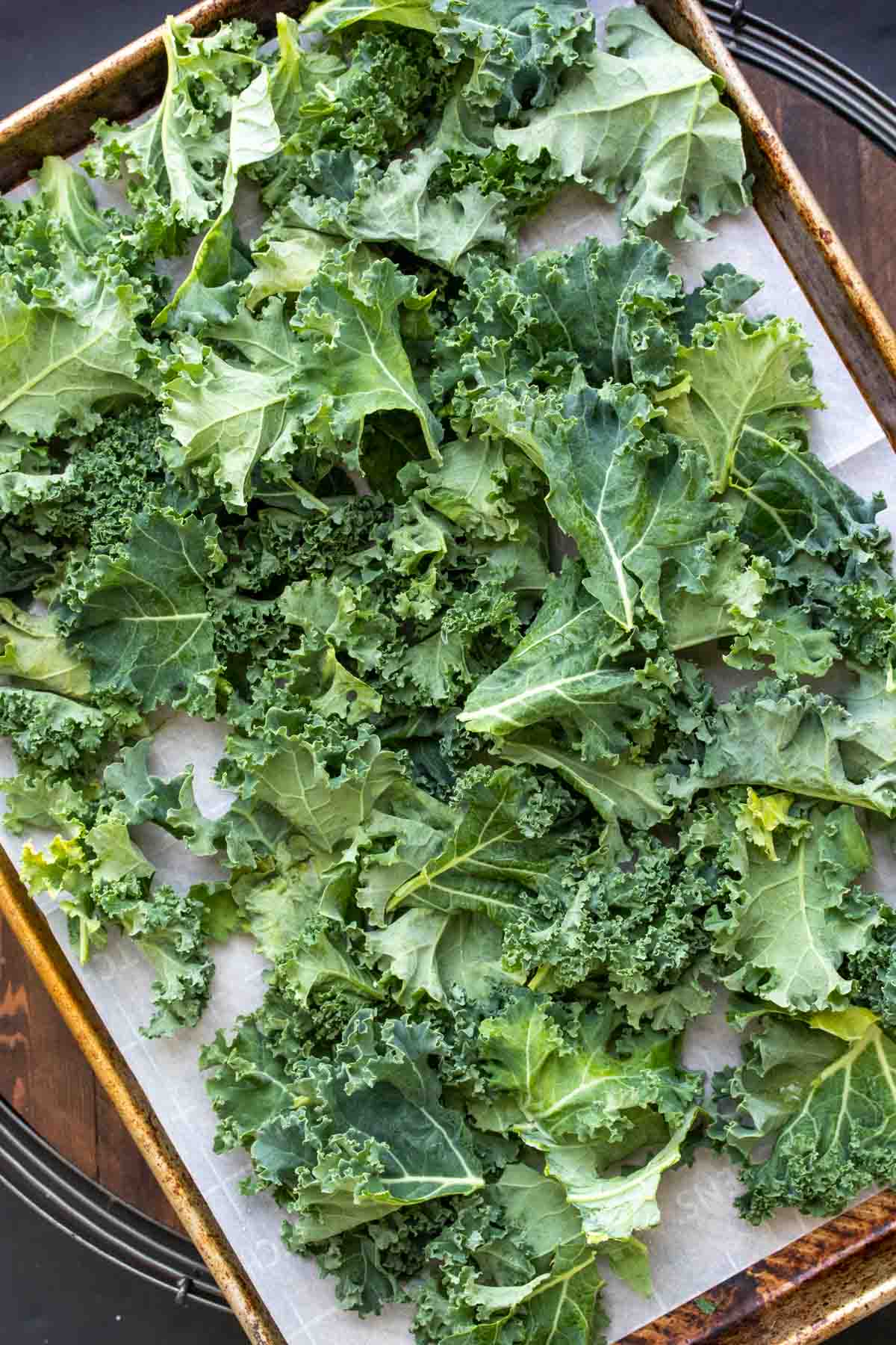 Cookie sheet with parchment and pile of kale pieces on top