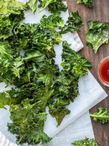 Pile of kale chips on a piece of parchment paper with dip nearby