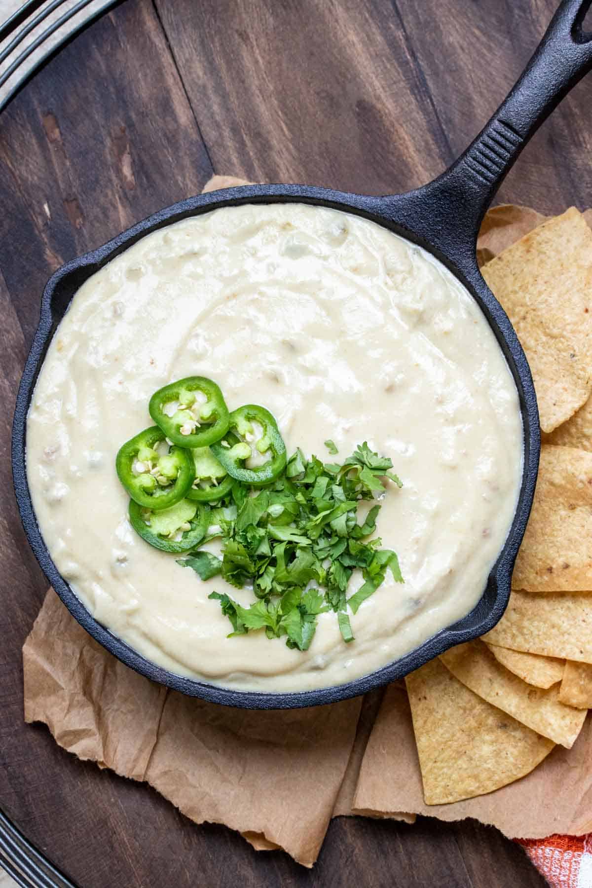 Top view of vegan white queso in skillet topped with sliced jalapeños and cilantro