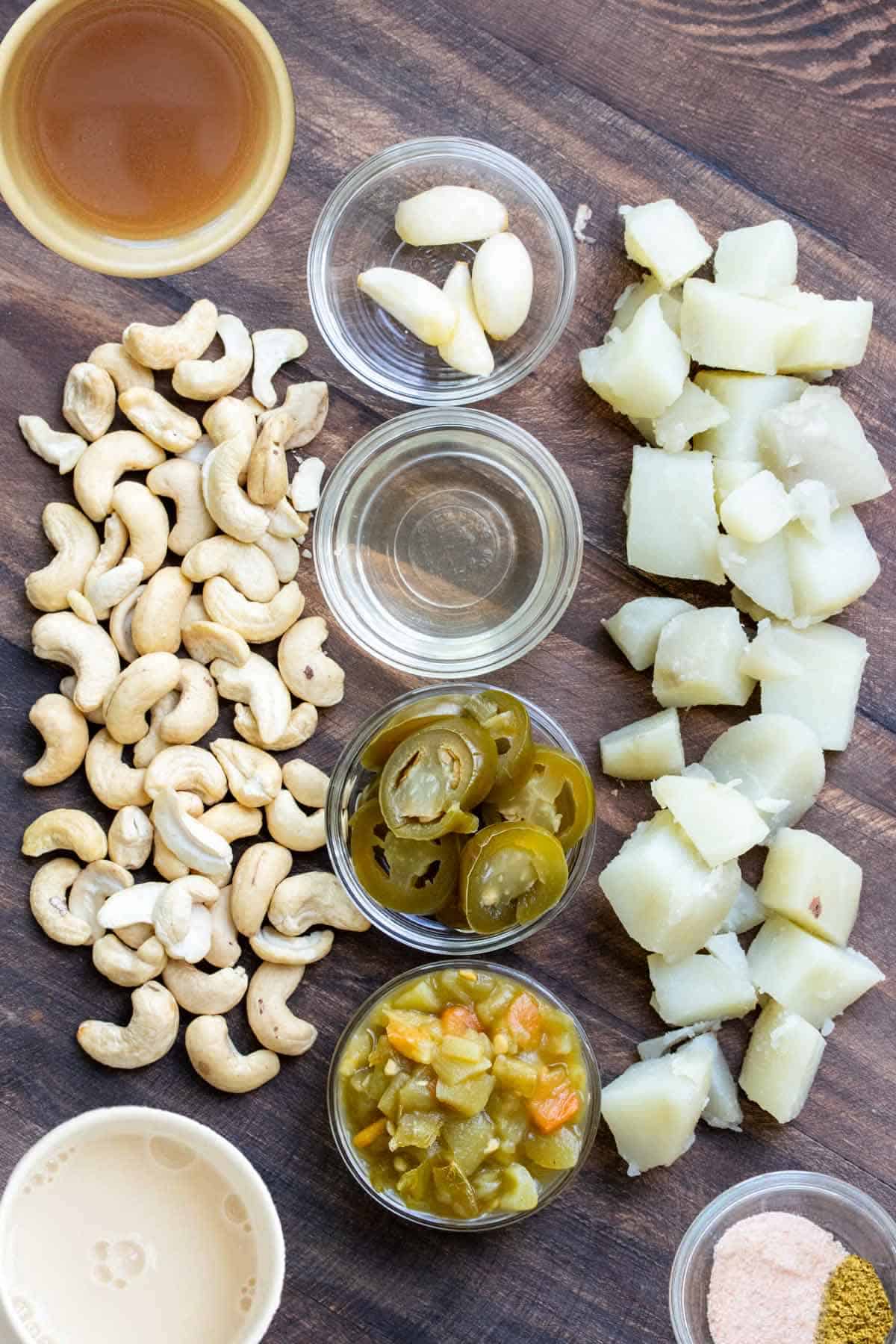 Pile of cashews and potatoes, and garlic, chiles, jalapeño slices and jalapeño juice in glass bowls