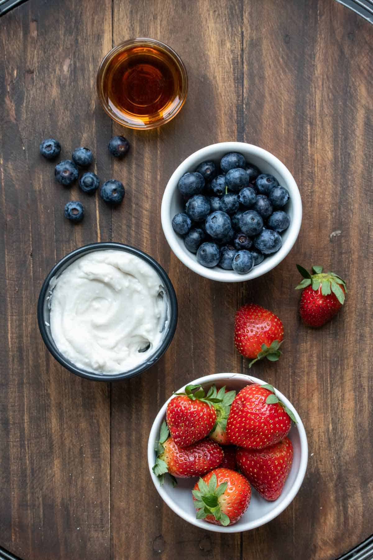 Bowls of fruit, yogurt and maple syrup on a wooden surface