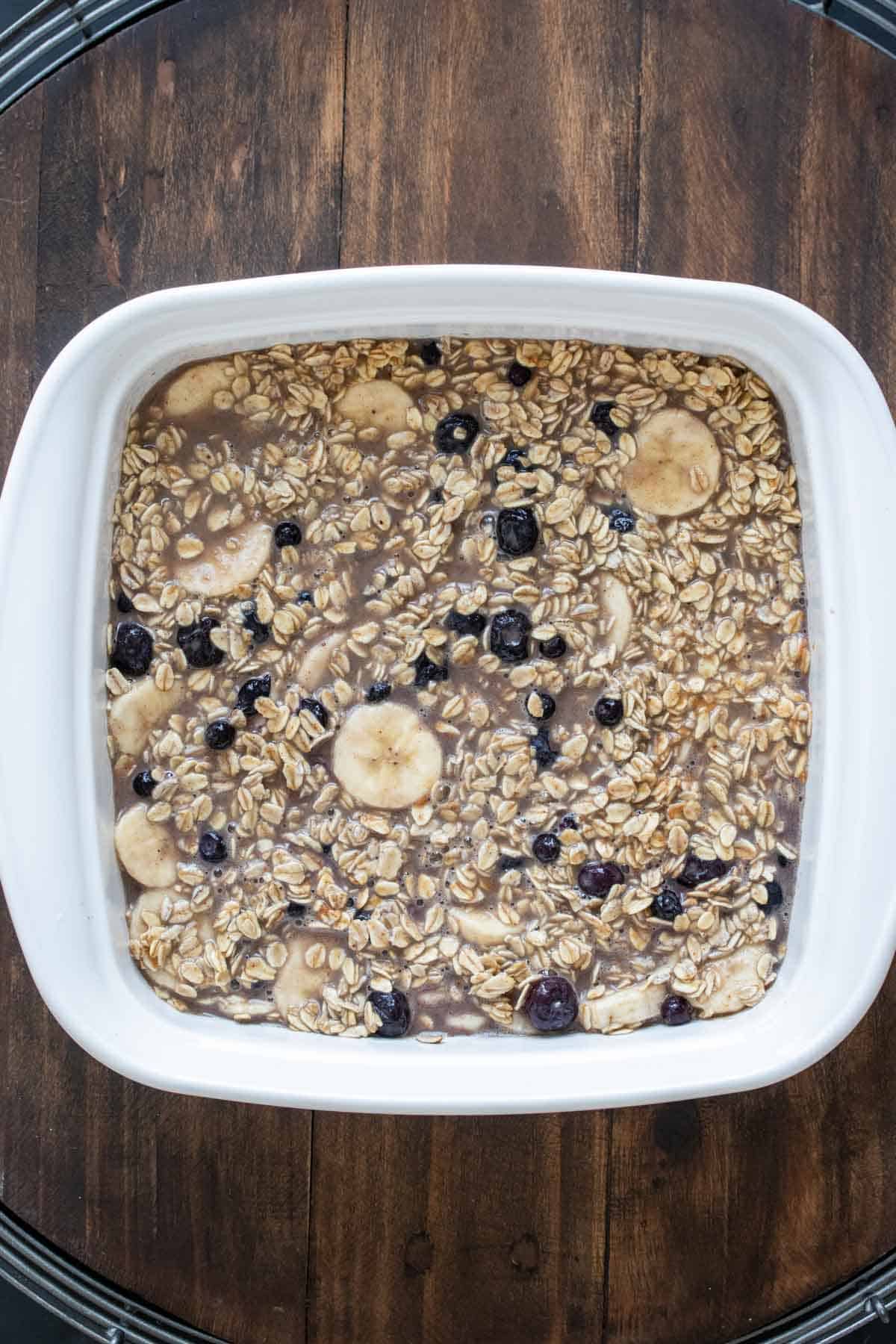 White baking dish filled with uncooked oats mixed with blueberries and banana slices