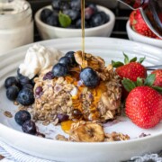 Pouring maple syrup on a piece of baked blueberry and banana oatmeal on a white plate