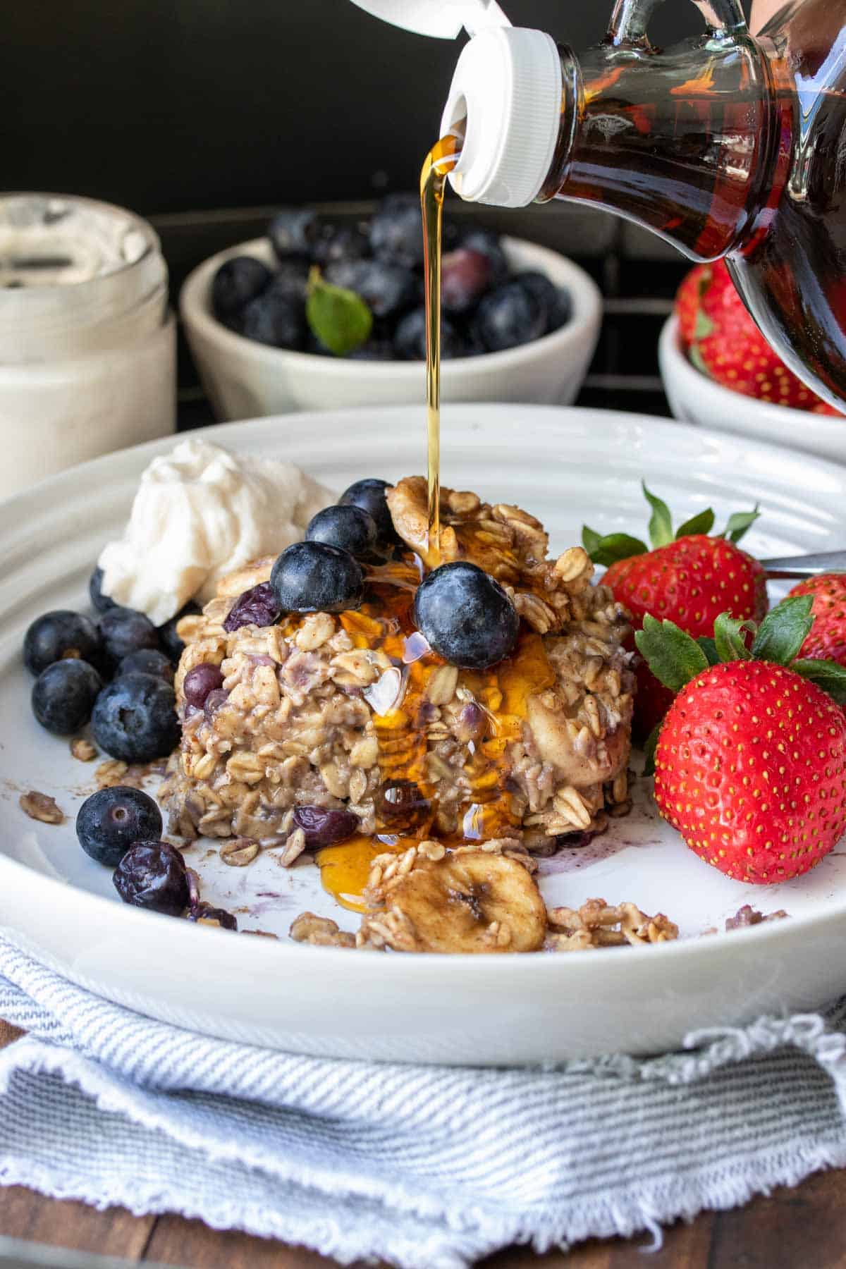 Pouring maple syrup on a piece of baked blueberry and banana oatmeal on a white plate