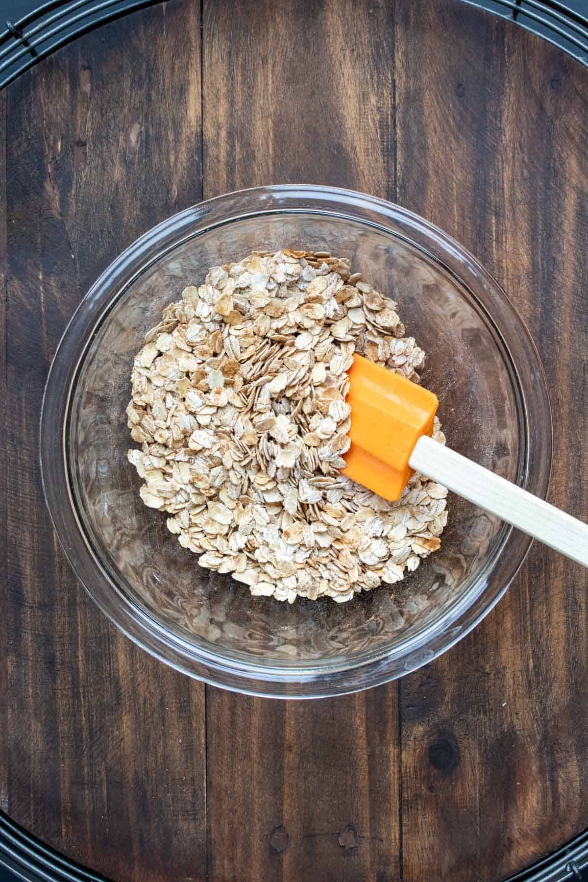 Glass bowl with oats being mixed with a orange spatula