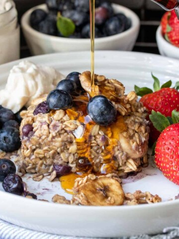 Fruit surrounding a piece of baked oatmeal with maple syrup being drizzled on it