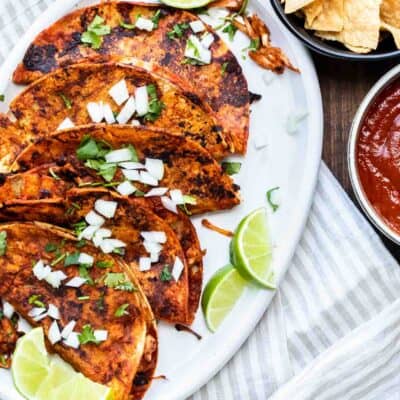 White platter with sauce covered pan fried tacos with toppings on it