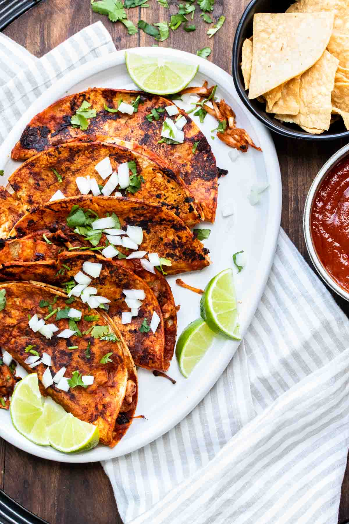 White platter with sauce covered pan fried tacos with toppings on it