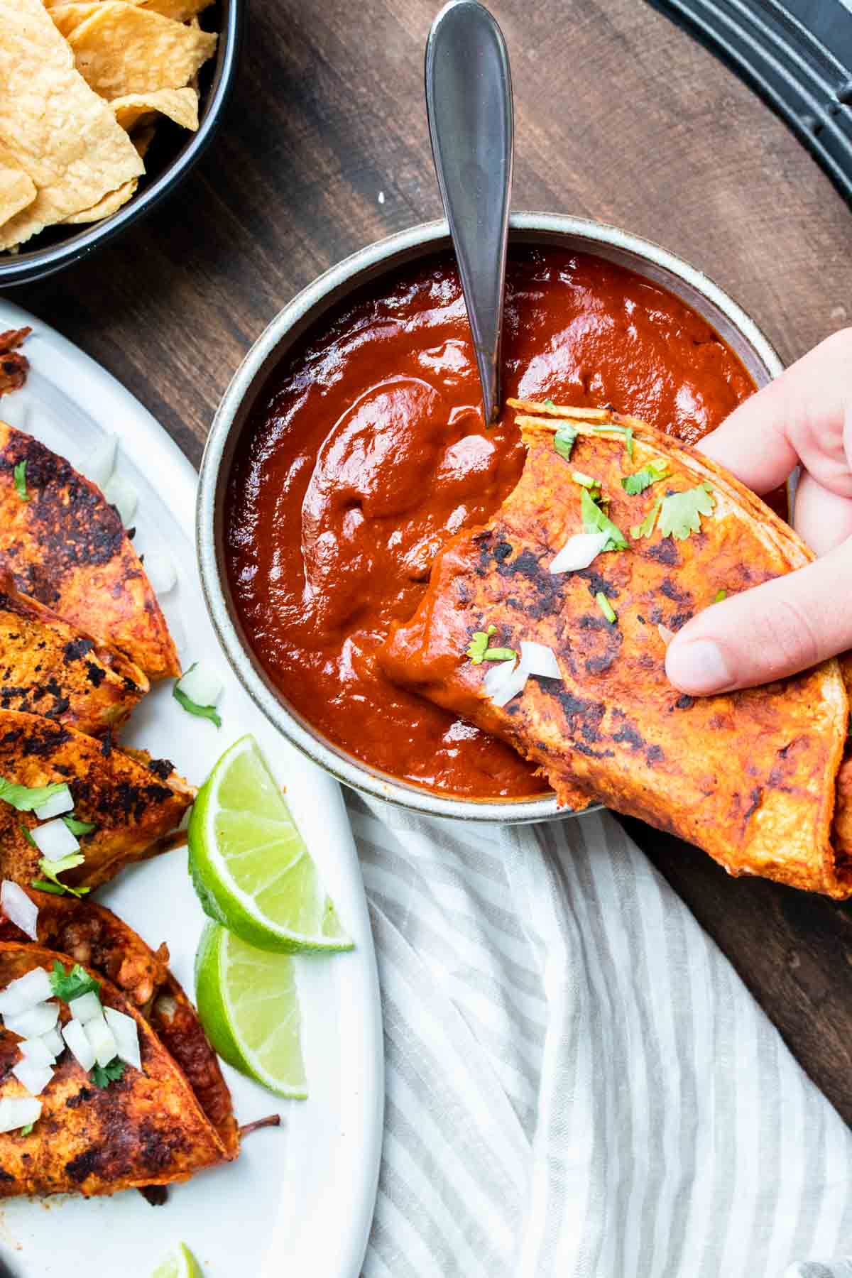 Hand dipping a fried red taco into red sauce