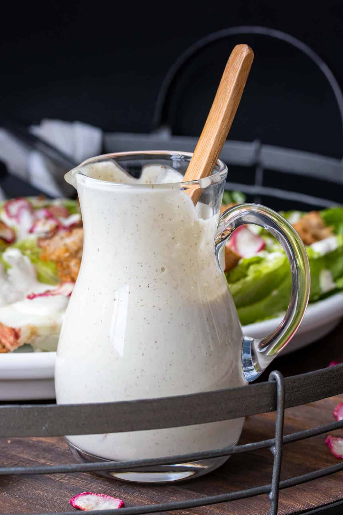 Glass pitcher jar filled with Caesar salad and a wooden spoon