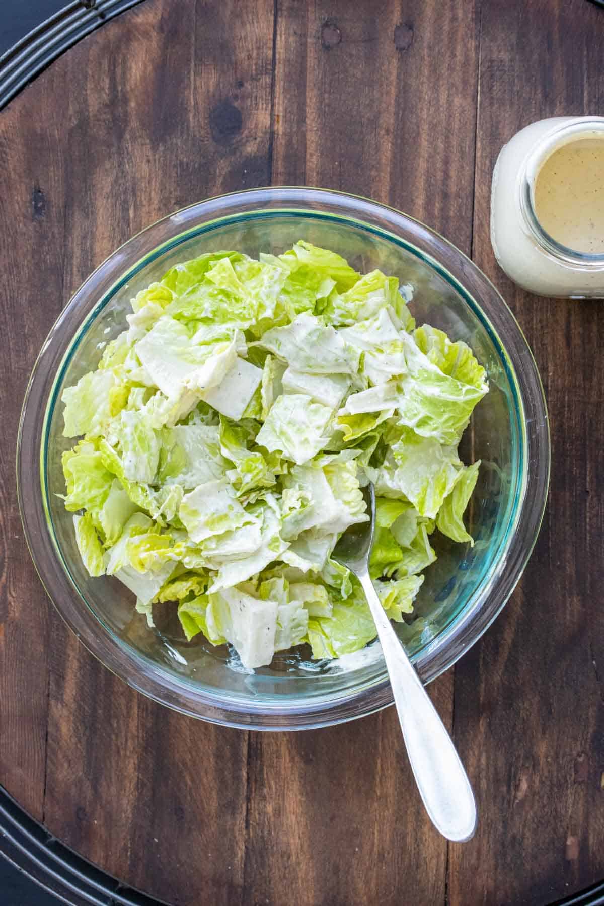 Glass bowl filled with chopped lettuce next to a bottle of dressing