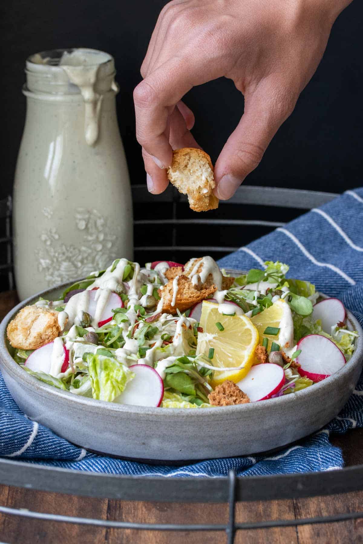 Hand putting croutons on a dressed salad with toppings