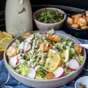 Grey plate with a dressed salad in front of bowls of toppings and dressing