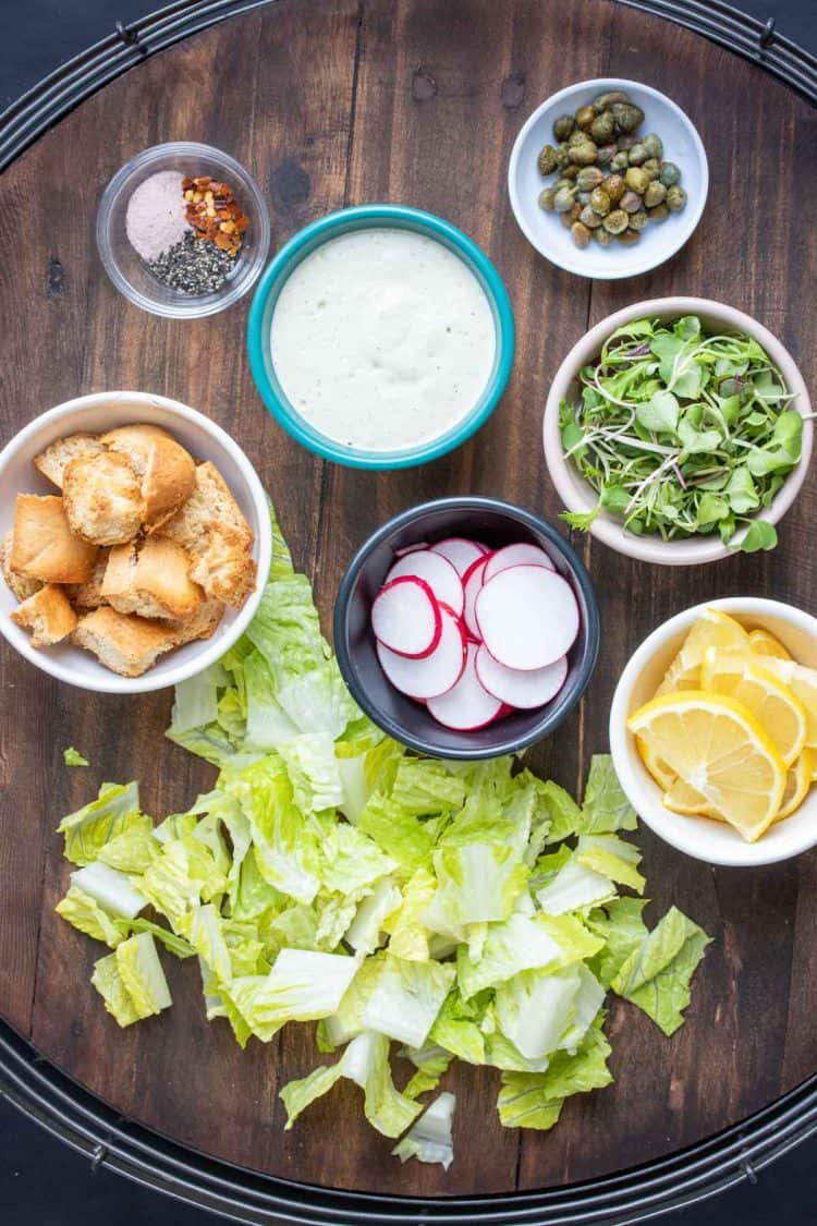 Wooden tray with chopped lettuce and toppings for a Caesar salad