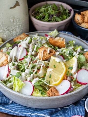 Grey plate with chopped lettuce and toppings drizzled with white dressing