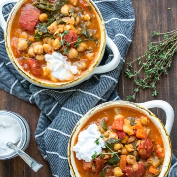 Two white soup bowls filled with a veggie and chickpea stew topped with yogurt
