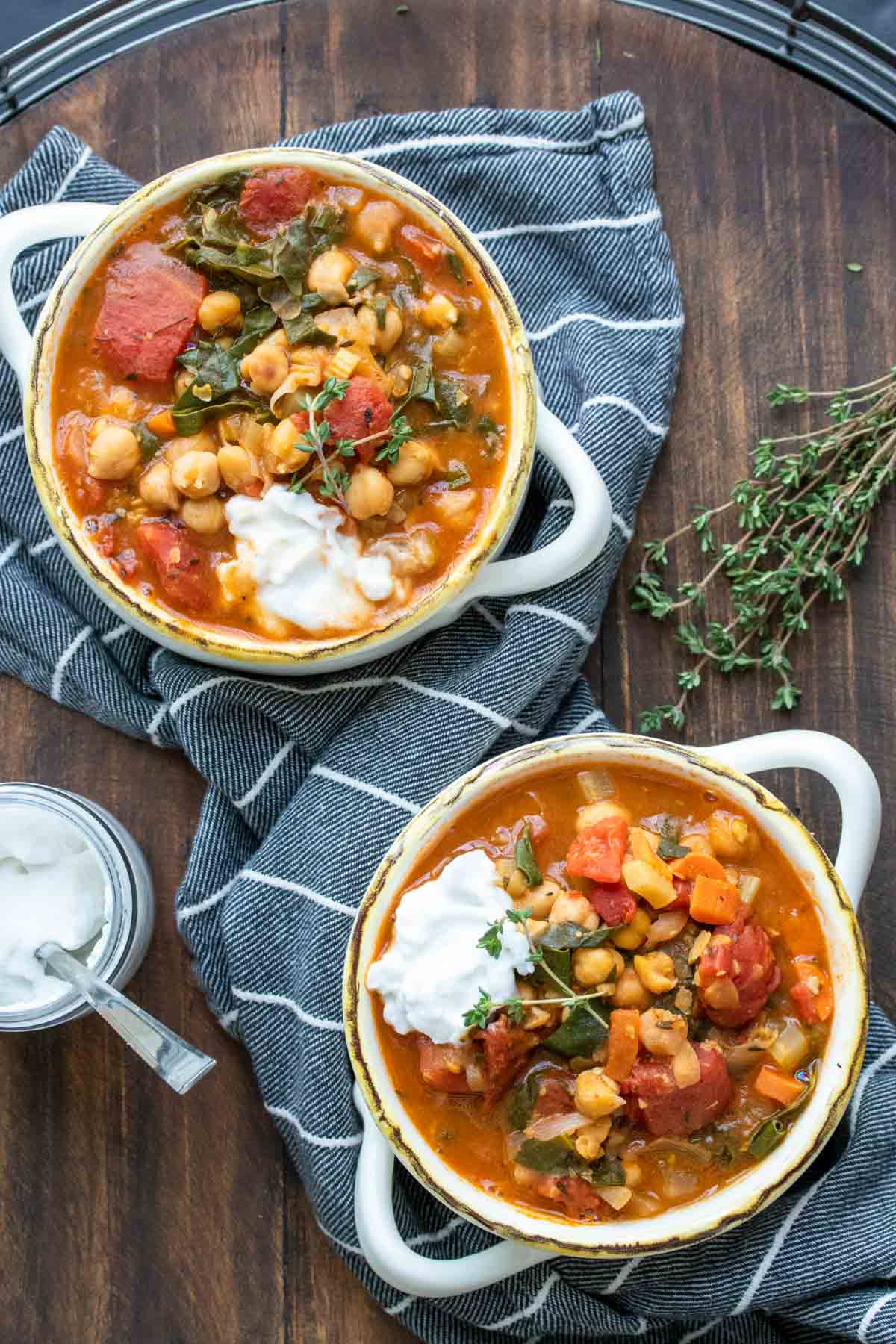 Two white soup bowls filled with a veggie and chickpea stew topped with yogurt.